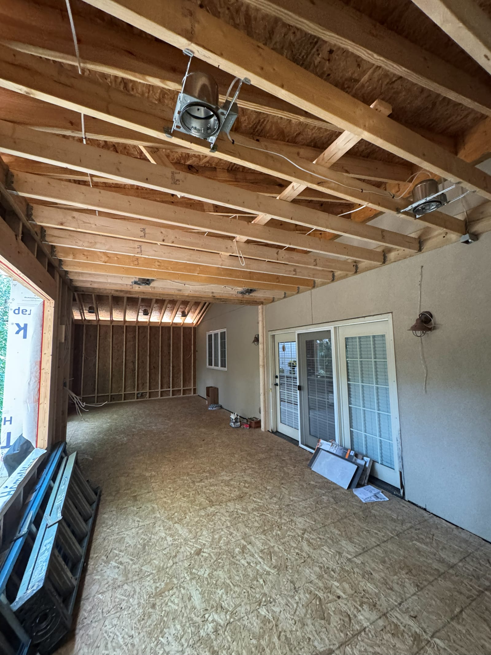 Room addition at rough-in stage with recessed light housings hung between the ceiling joists and cable runs stapled to the framing