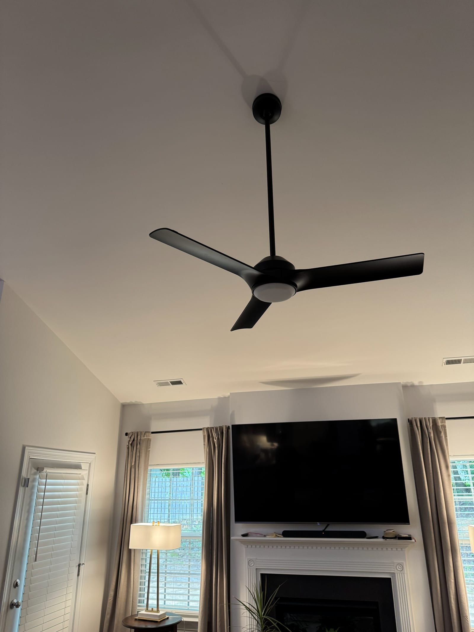 Modern black three-blade ceiling fan on a downrod installed in a vaulted living room ceiling