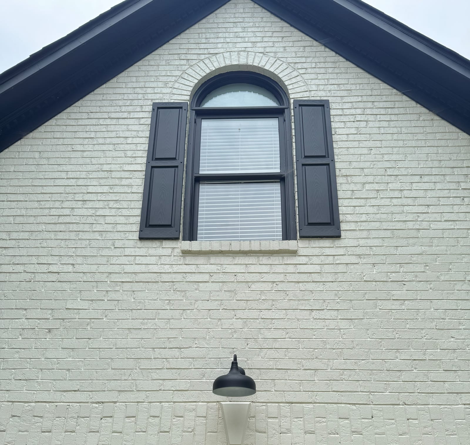 Black gooseneck barn light mounted on a white painted brick gable above a garage