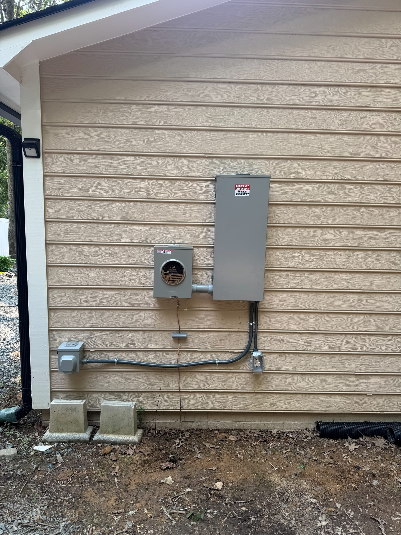 New electric meter base and outdoor service disconnect installed on the side of a house, with conduit run to a weatherproof outlet
