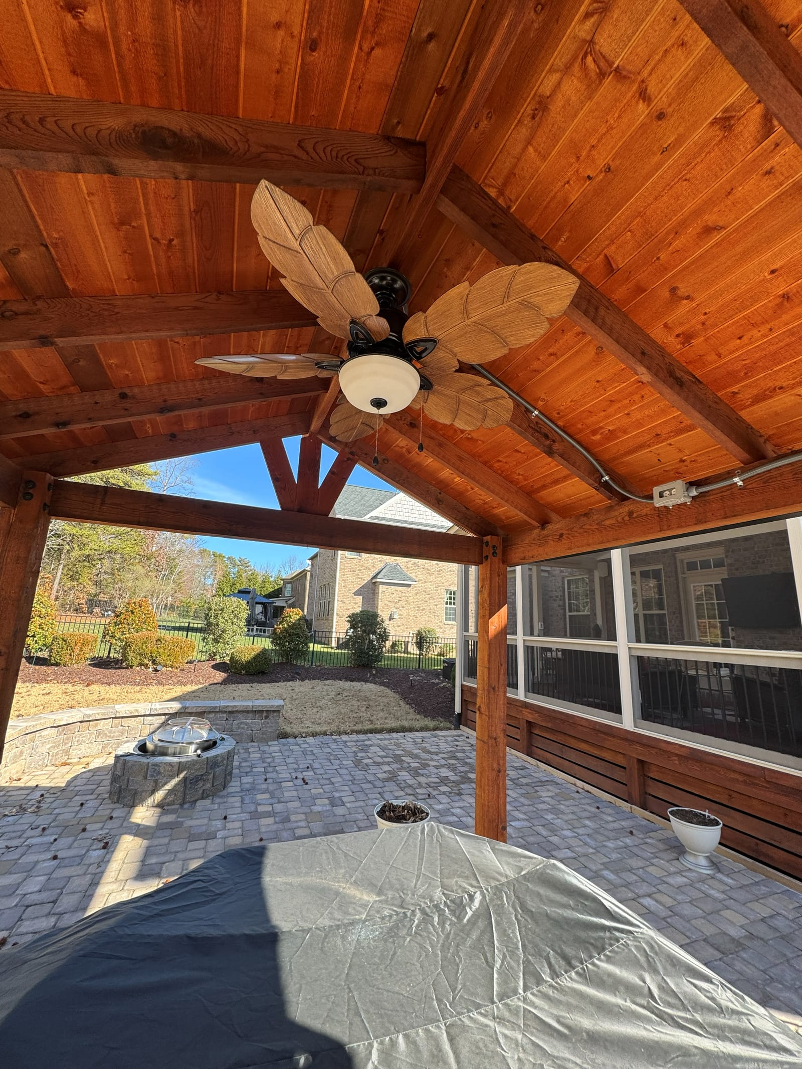 Ceiling fan installed in a stained timber vaulted patio roof, overlooking a paver patio and fire pit