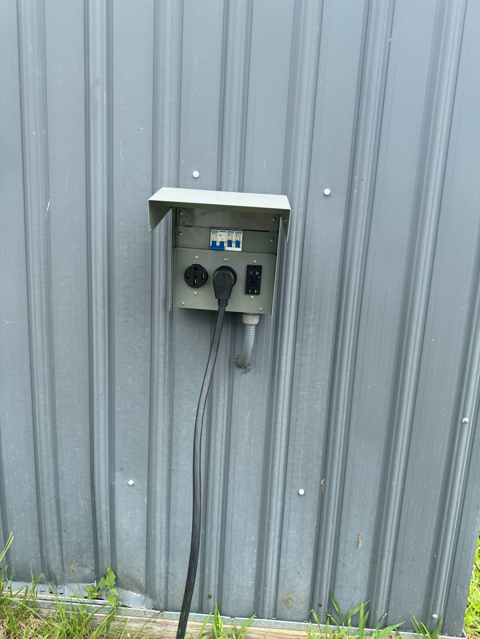 Weatherproof outdoor power outlet box with a 50-amp RV receptacle, 30-amp receptacle and GFCI outlet, mounted on a metal building