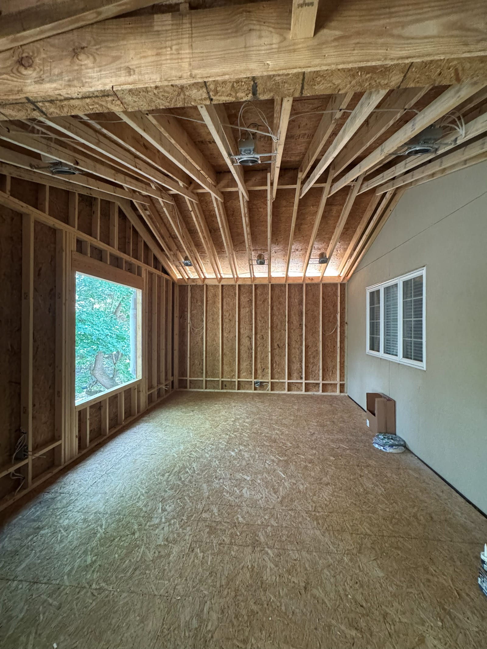 Vaulted room addition at rough-in stage with a row of recessed light housings mounted in the rafters